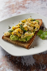 Toasted slice of bread topped with avocado and scrambled eggs. Healthy toast (tartine).