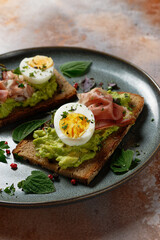 Toasted slice of bread topped with avocado, a hard-boiled egg and ham. Healthy toast (tartine).