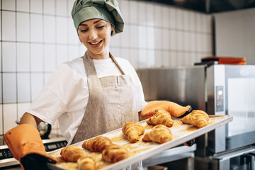 Female baker at the kitchen holding freshly baked croiisants