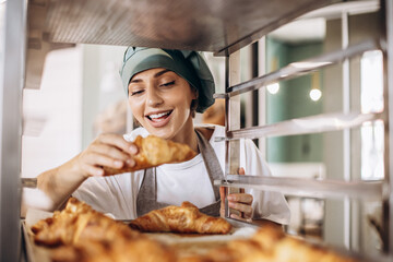 Female baker at the kitchen holding croissant