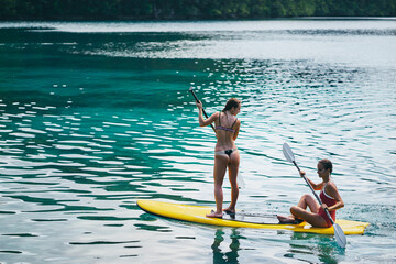 Summer holidays vacation travel. SUP Stand up paddle board. Young women sailing together on beautiful calm lagoon. - obrazy, fototapety, plakaty