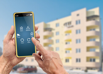 Male hands holding mobile phone with smart home application on screen over apartment building...