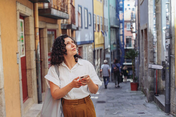 Lost woman in casual clothes walking on an old European street, looking around, using a map on her smartphone 