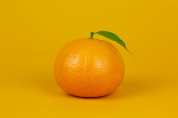 An Orange fruit with green leaf isolated on yellow background. One orange fruit with leaf stand on isolating concept for ads design