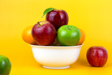 An organic healthy fruits, green apples, red apple, oranges isolated on yellow background. Healthy fruits in a white bowl on yellow background. used for cooking concepts