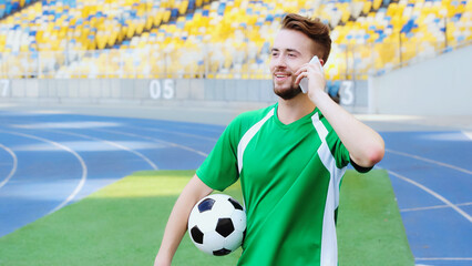 smiling football player holding ball and talking on smartphone