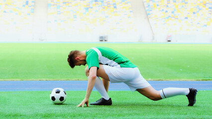 young football player in uniform stretching legs on green grass bear soccer ball © LIGHTFIELD STUDIOS