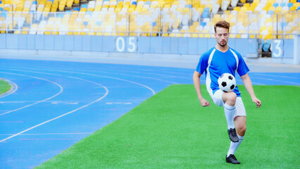 young football player bouncing soccer ball with legs on stadium