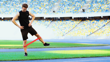 full length of bearded sportsman with hands on hips exercising with resistance band