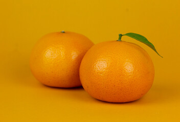 Two Oranges fruits with green leaf isolated on yellow background. One orange fruit with leaf stand on isolating concept