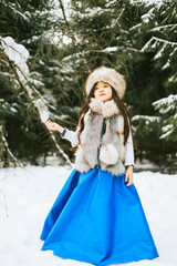 Fototapeta premium portrait of beautiful cute little Asian girl in fur coat and fur hat standing in snowy forest in winter, winter holidays and having fun, Christmas vacation