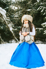 portrait of beautiful cute little Asian girl in fur coat and fur hat standing in snowy forest in winter, winter holidays and having fun, Christmas vacation