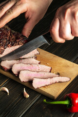 The chef cuts the baked beef meat into small pieces on the cutting board of the kitchen. Top view cooking process concept.