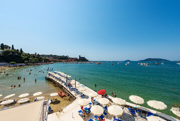 Beach of Lerici Town with many umbrellas, tourist resort on the coast of the Gulf of La Spezia or Gulf of Poets, Liguria, Italy, Europe. Islands of Tino, Tinetto and Palmaria, and Porto Venere town. - obrazy, fototapety, plakaty
