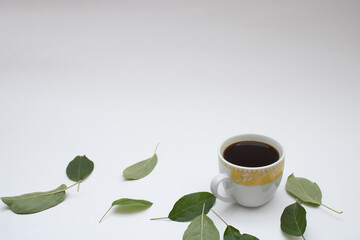 White-yellow cup of coffee with green leaves laid on white background. Minimal concept.