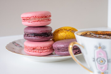 Mix of appetizing macarons on plate on white background with black coffee in porcelain cup in foreground.