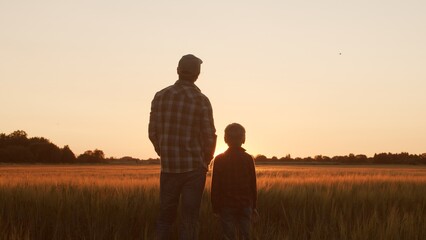 Farmer and his son in front of a sunset agricultural landscape. Man and a boy in a countryside...