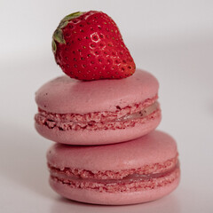 Appetizing pink macarons with juicy strawberry on top on white background.