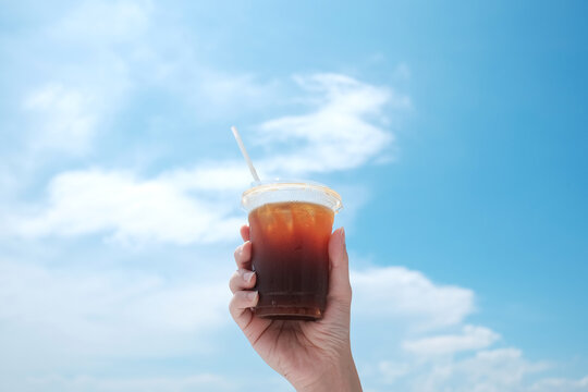 hand holding iced coffee cup with blue sky