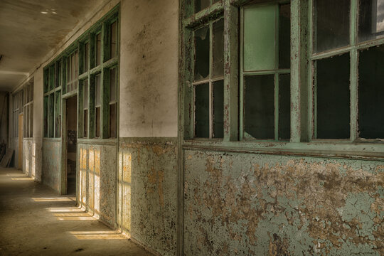 Lost place hallway in an old barracks with door and broken windows and peeling wall paint in pastel colors and light through windows with window crosses