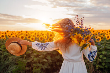 Happy woman walking in blooming sunflower field at sunset having fun holding bouquet of flowers....