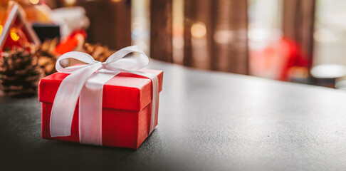 Red christmas gift box with white ribbon on table against bokeh background. Соpy space