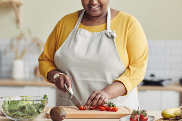 Cropped portrait of black woman cooking healthy meal in kitchen and cutting vegetables
