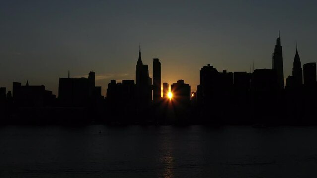 slow trucking shot along silhouetted buildings at gorgeous sunset, at the tail end of the rare Manhattanhenge phenomenon.  A small sun glimpse peeks through the legendary skyline