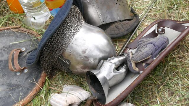 Medieval wrought iron armor and helmet lie on the grass at the festival of historical reenactment reconstruction .