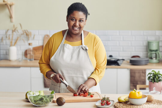Waist up portrait of young black woman cooking healthy salad in kitchen and cutting vegetables, copy space