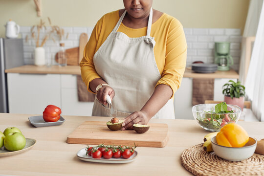 Cropped portrait of black woman cutting avocado while cooking healthy meal in kitchen, copy space