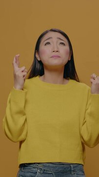 Vertical video: Positive adult doing praying sign with fingers crossed, asking and wishing for good luck and fortune in isolated background. Hopeful person expressing desire and wishful thinking.