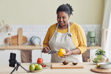 Portrait of young black woman cooking healthy meal in kitchen and recording video, copy space