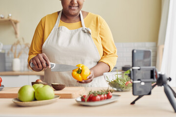 Closeup of young black woman cooking healthy meal in kitchen and recording video with smartphone,...