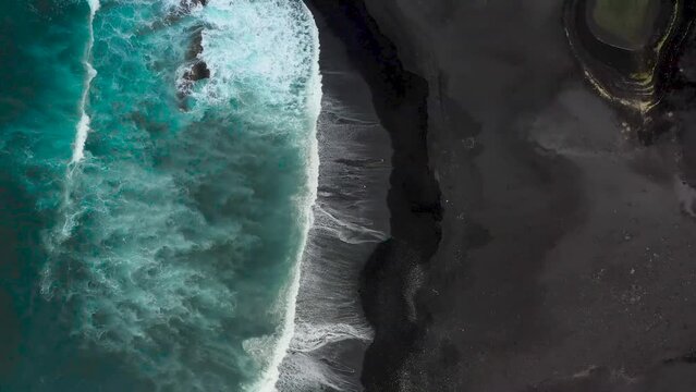 Blaues Meer und schwarzer Strand mit der Drohne gefilmt. Ein P&auml;rchen l&auml;uft am schwarzen Strand entlang. Vogelperspektive am Strand. 2