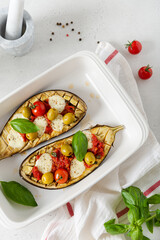 Grilled eggplants with mozzarella, tomatoes, basil and olives in baking dish on white background. Aubergine seasonal vegan recipe. Dieting, healthy nutrition. Restaurant menu. top view, close up