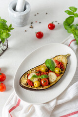 Italian traditional dish with eggplant, tomatoes, olives, mozzarella and basil. Baked aubergine stuffed with vegetables on a white plate. Vegan menu recipe. Top view.