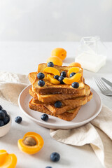Delicious french toasts with fresh fruits and berries and maple syrup. Tasty breakfast dessert with toast, apricots and blueberries on white background. Copy space. Recipe, menu