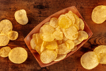 Potato chips or crisps, a salty snack in a bowl, overhead flat lay shot on a rustic wooden background