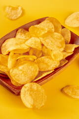 Potato chips or crisps in a bowl and scattered on a yellow background, a salty snack