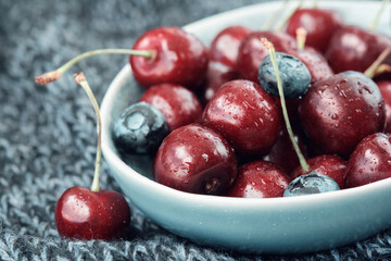Bowl full of ripe red cherries on a dark blue knitted blanket.