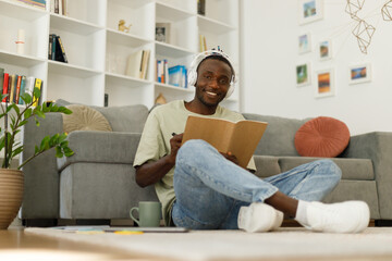 Remote education. Cool black teenager taking notes in a notebook and looking at the camera at home, full length