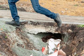 a man's feet jump over a pit next to an asphalt sidewalk.