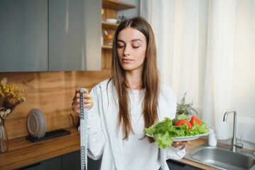 Happy young woman preparing salad in kitchen. Healthy diet