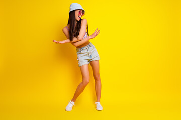 Full length photo of funky charming girl dressed swimsuit bra cap dark eyewear dancing empty space isolated yellow color background