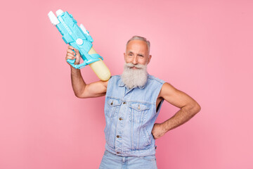 Photo of cool attractive man pensioner dressed denim vest holding water gun isolated pink color...