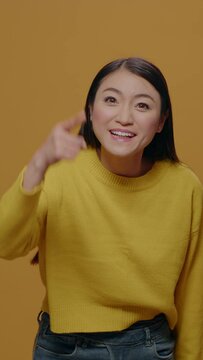 Vertical video: Furious adult arguing in front of camera, raising finger in frustration, standing over yellow background. Irritated woman having argument and aggressive reaction, showing indignation.