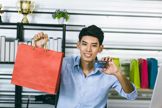 A young Asian influence male vlogger holding a shopping bag and a credit card while live streaming, youtuber concept.