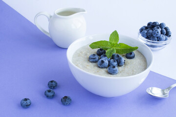 Oatmeal with milk and blueberry in the white bowl on the purple background. Healthy breakfast. Closeup.