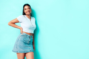 Young beautiful smiling female in trendy summer jeans skirt and top clothes. Carefree woman posing near blue wall in studio. Sexy positive model having fun indoors. Cheerful and happy